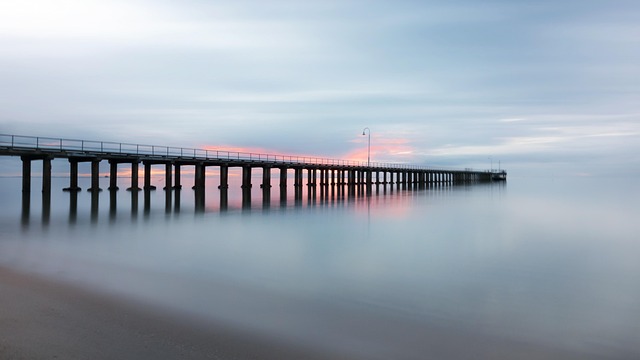 Wooden pier stretching into a calm sea at dusk, fog over water